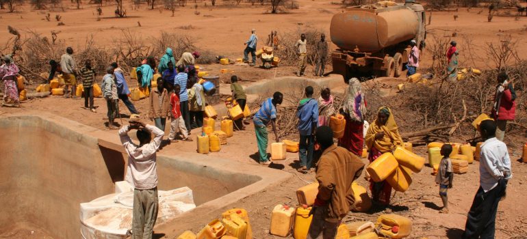 A dried up water distribution with many people with jerrycans waiting for water